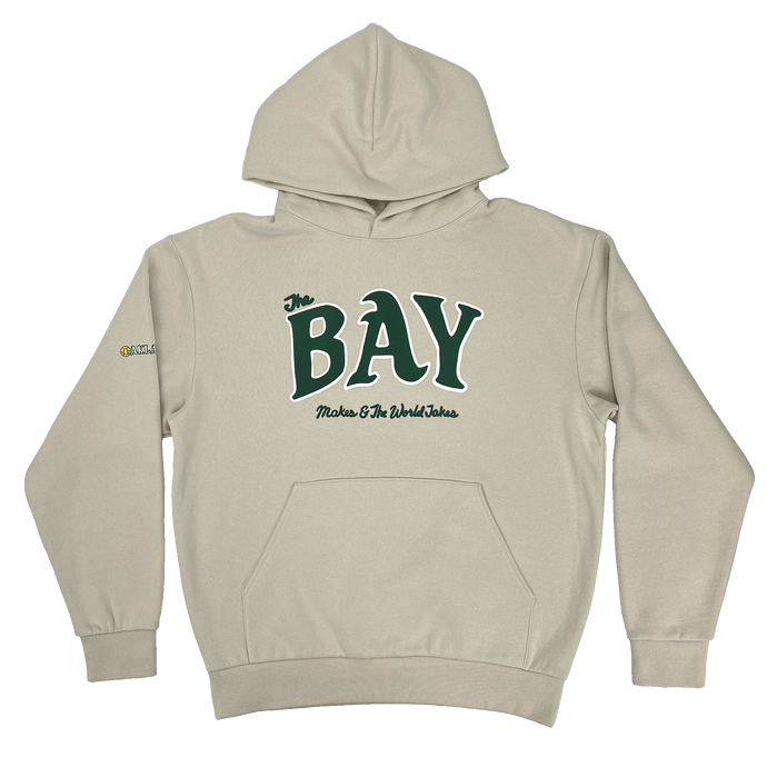 Front view of an ivory pullover hoodie sweatshirt with large green The Bay Makes, The World Takes logo on the front chest.