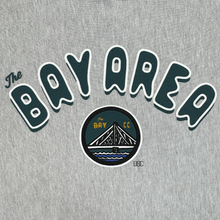 Load image into Gallery viewer, The Bay Area CC Hoodie by DOC from Oaklandish is a gray men’s pullover featuring “The Bay Area” in dark green outlined in white and a circular emblem with a bridge, “The Bay,” and “CC” in yellow for San Francisco Bay Area pride.