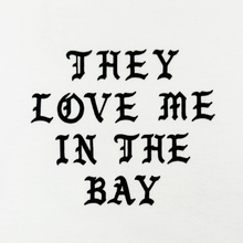 Load image into Gallery viewer, The They Love Me LS Tee By Doc by By DOC features bold, black gothic-style text that reads “THEY LOVE ME IN THE BAY,” centered and evenly spaced across three lines on a crisp white heavyweight cotton long sleeve t-shirt. Designed with men’s sizing, it combines standout style with exceptional comfort.